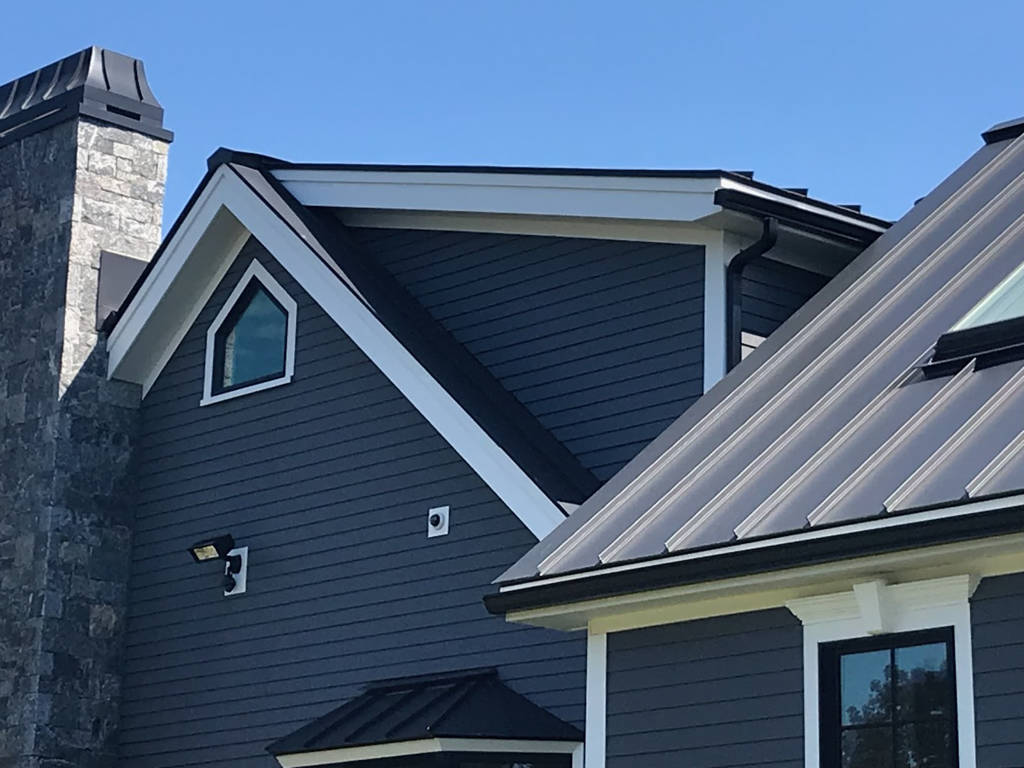 A blue house with a chimney and a grey metal roof in CT, MA, NH, or RI