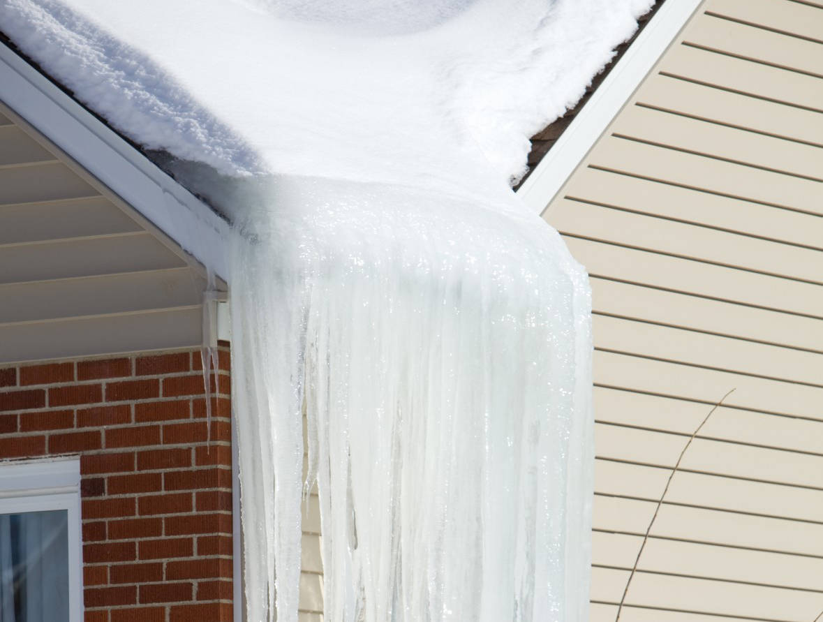 A closeup of an ice dam with icicles hanging off of a roofline.