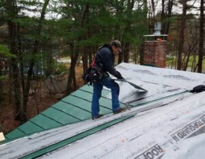 A man working on a green metal roof in MA CT NH RI