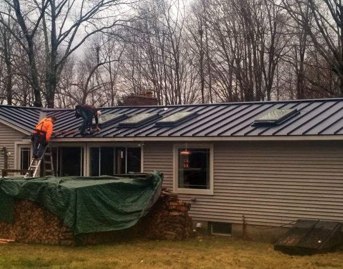 Metal roof being worked on next to piles of logs in CT MA RI NH