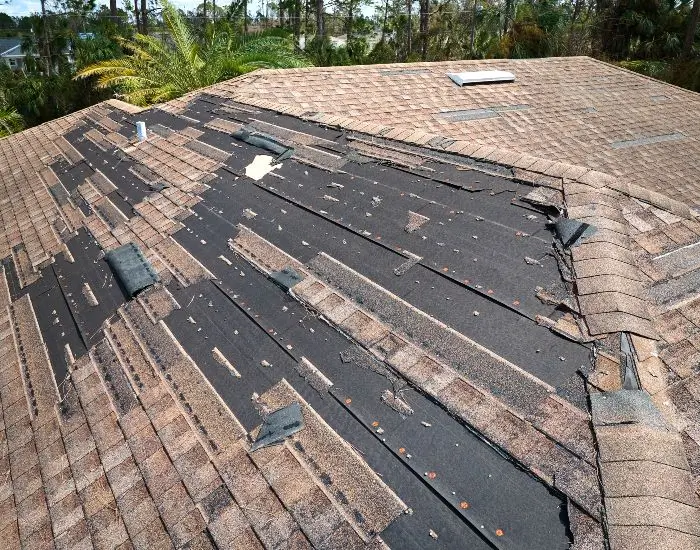 A roof with brown shingles shows damage after a storm.