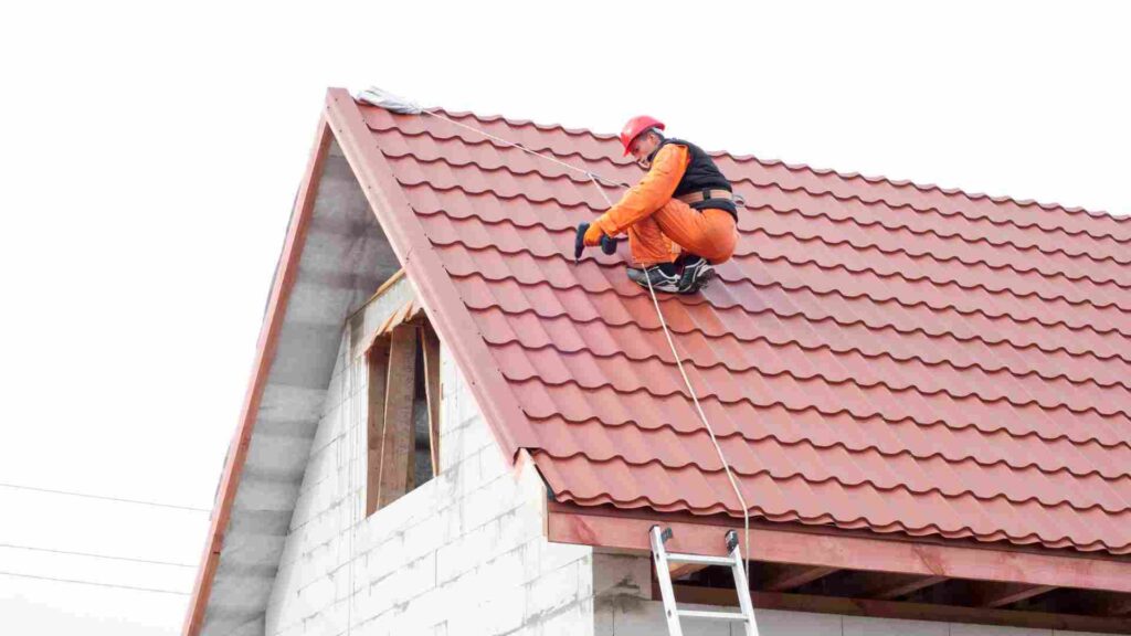 A man standing on a ladder, working on the roof of a house under clear blue skies.