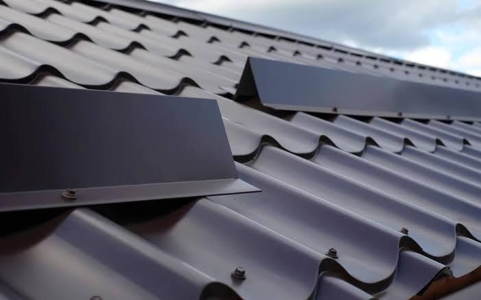 A close-up shot of a dark brown corrugated metal tile roof equipped with staggered metal snow guards.